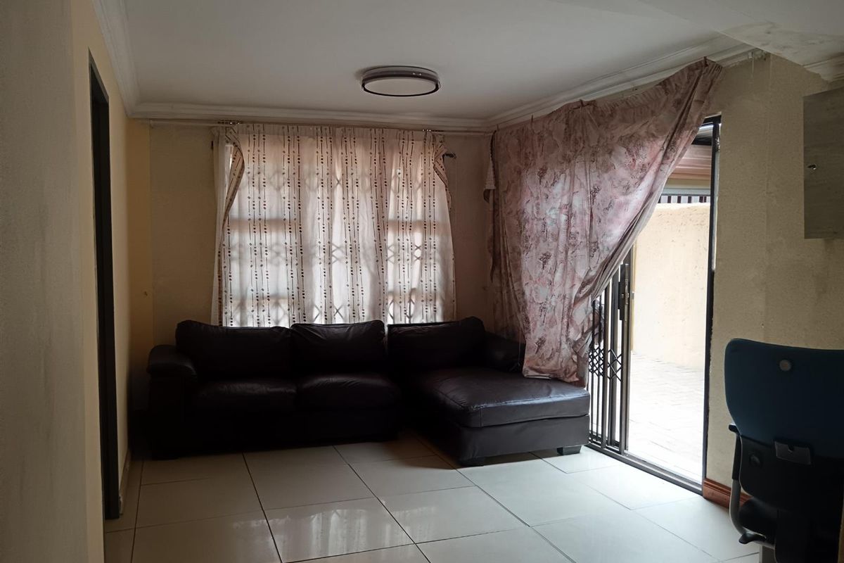 A living room featuring tiled flooring and a sliding glass door providing access to the exterior, with visible wear on the ceiling and walls.