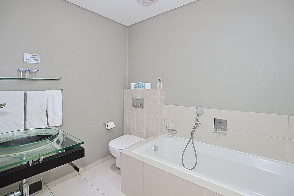 A modern bathroom featuring a built-in bathtub with handheld shower, wall-mounted toilet, and a glass vessel sink vanity.