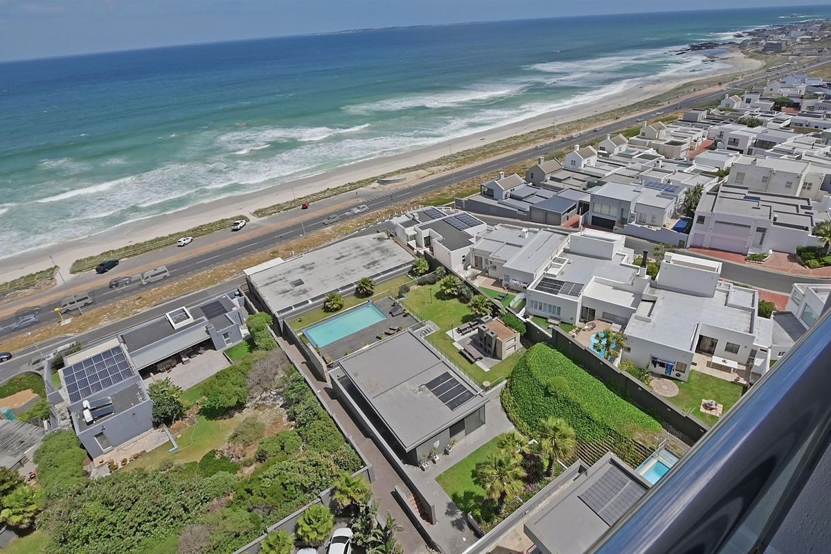 An elevated aerial view showcasing the coastal neighborhood, beach, and surrounding residential properties with clear ocean vistas.