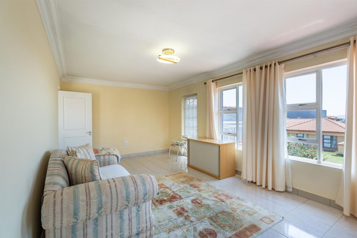 A bright living room featuring tiled flooring, crown molding, and large windows that provide natural light and views of the surrounding neighborhood.