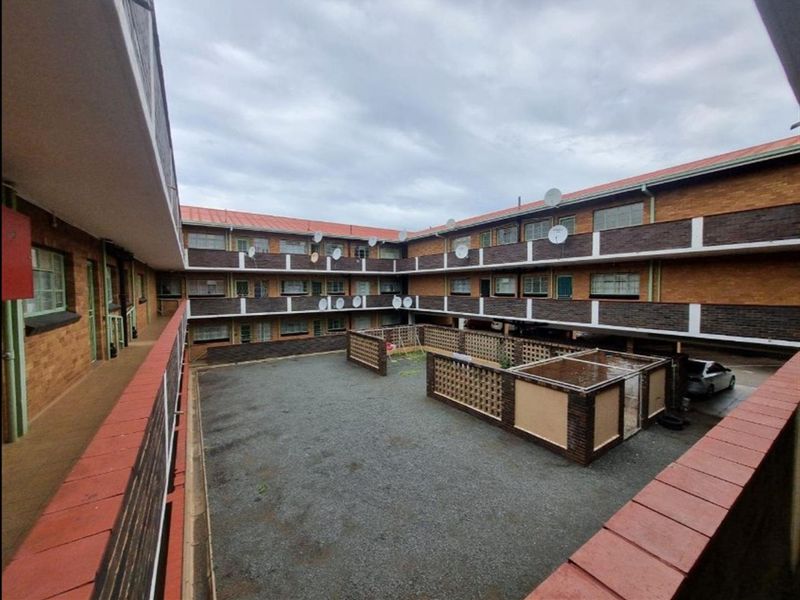 An elevated view of a multi-story residential complex featuring brick facades, metal roofing, and a central gravel courtyard with low brick boundary walls.