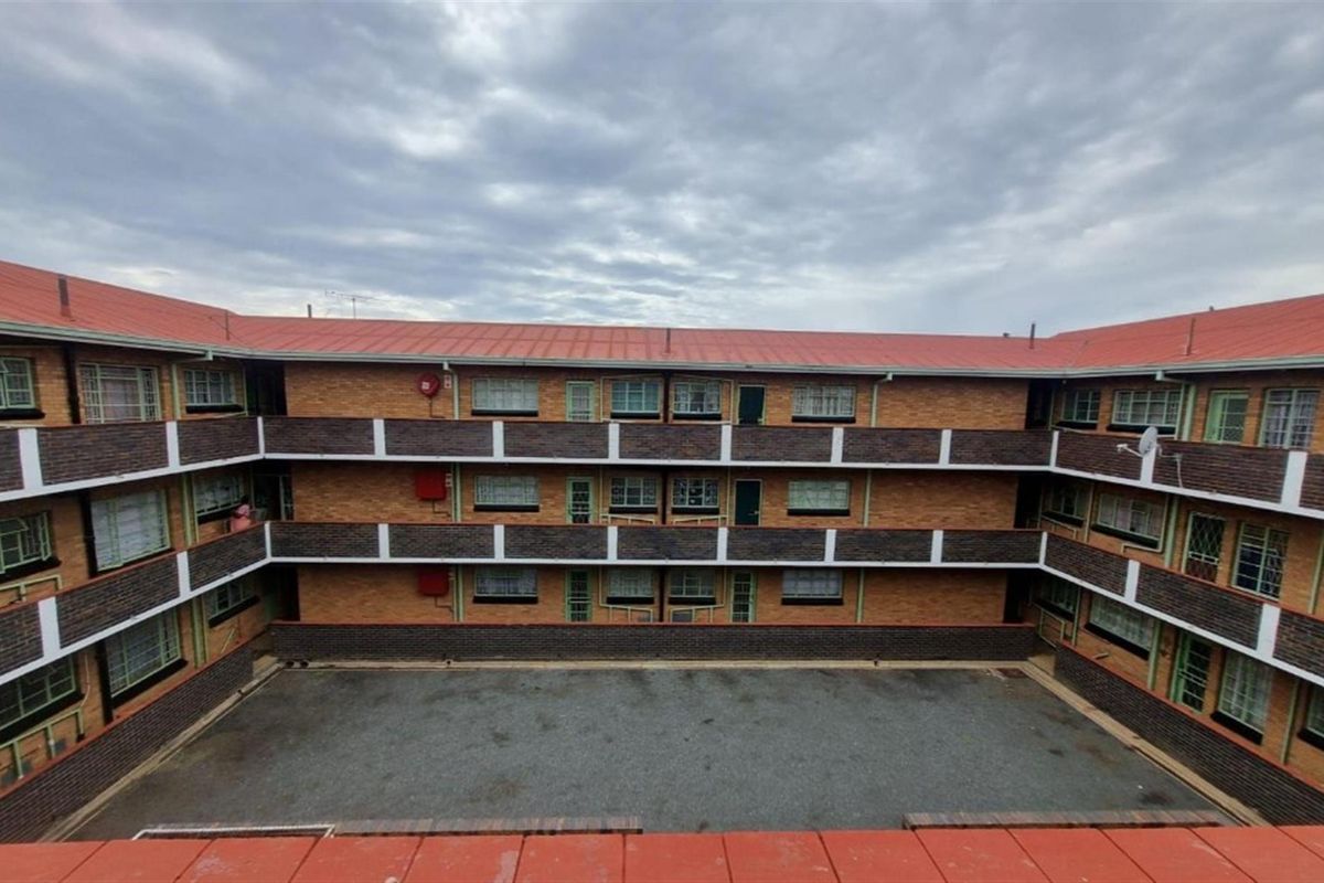 A multi-story residential building featuring a central paved courtyard, brick facade, and metal roofing with accessible balcony walkways.