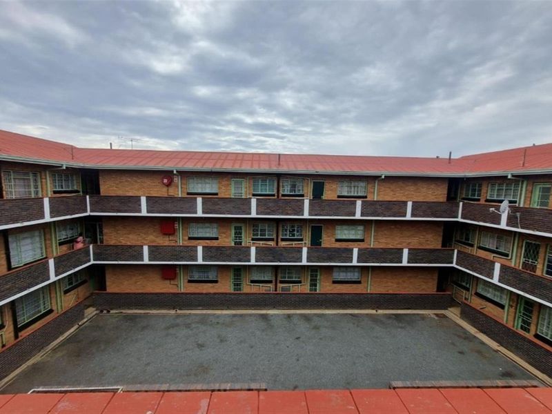 A multi-story residential building featuring a central paved courtyard, brick facade, and metal roofing with accessible balcony walkways.