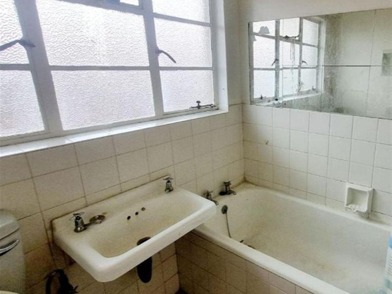 A dated bathroom featuring a wall-mounted basin, built-in bathtub, and tiled finishes, requiring modernization and refurbishment of fixtures.