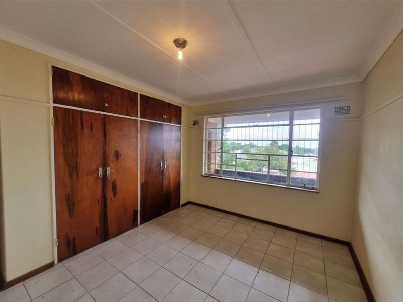 An empty bedroom featuring tiled flooring, built-in wooden cupboards, and a window with security bars, offering a functional space ready for personalization.