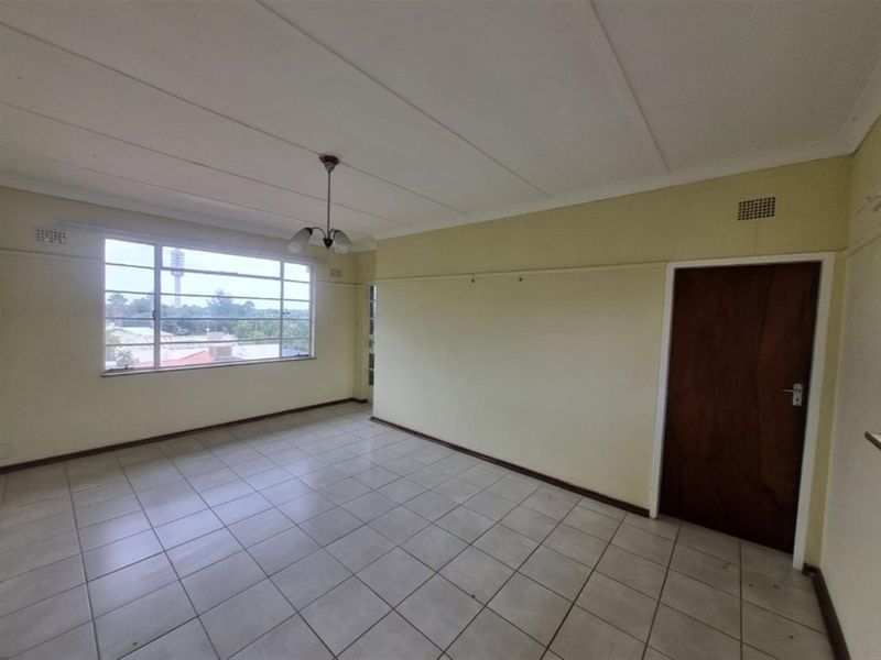 An empty living room featuring tiled flooring, a large window with exterior views, and a classic wooden door.