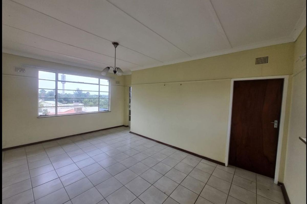 An empty living room featuring tiled flooring, a large window with exterior views, and a classic wooden door.