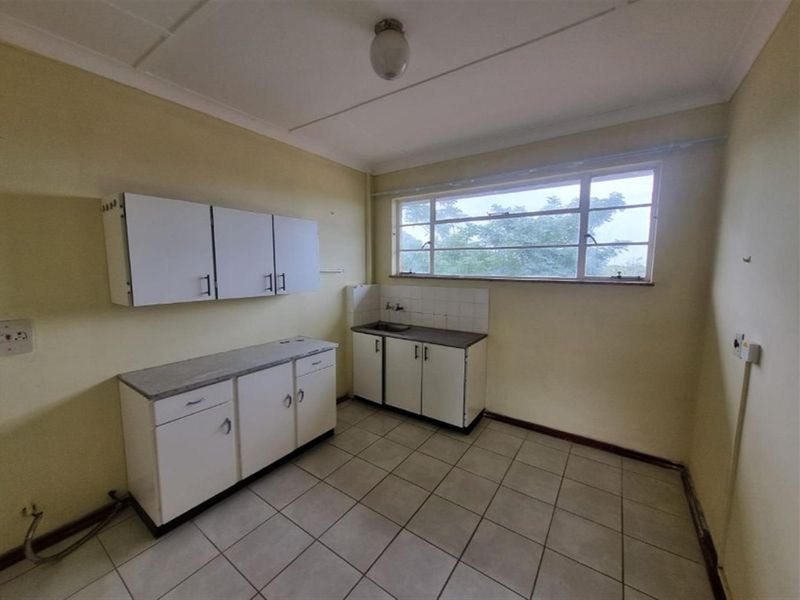 A functional, empty kitchen space featuring basic built-in cabinetry, a stainless steel sink, and tiled flooring, ready for a modern renovation.