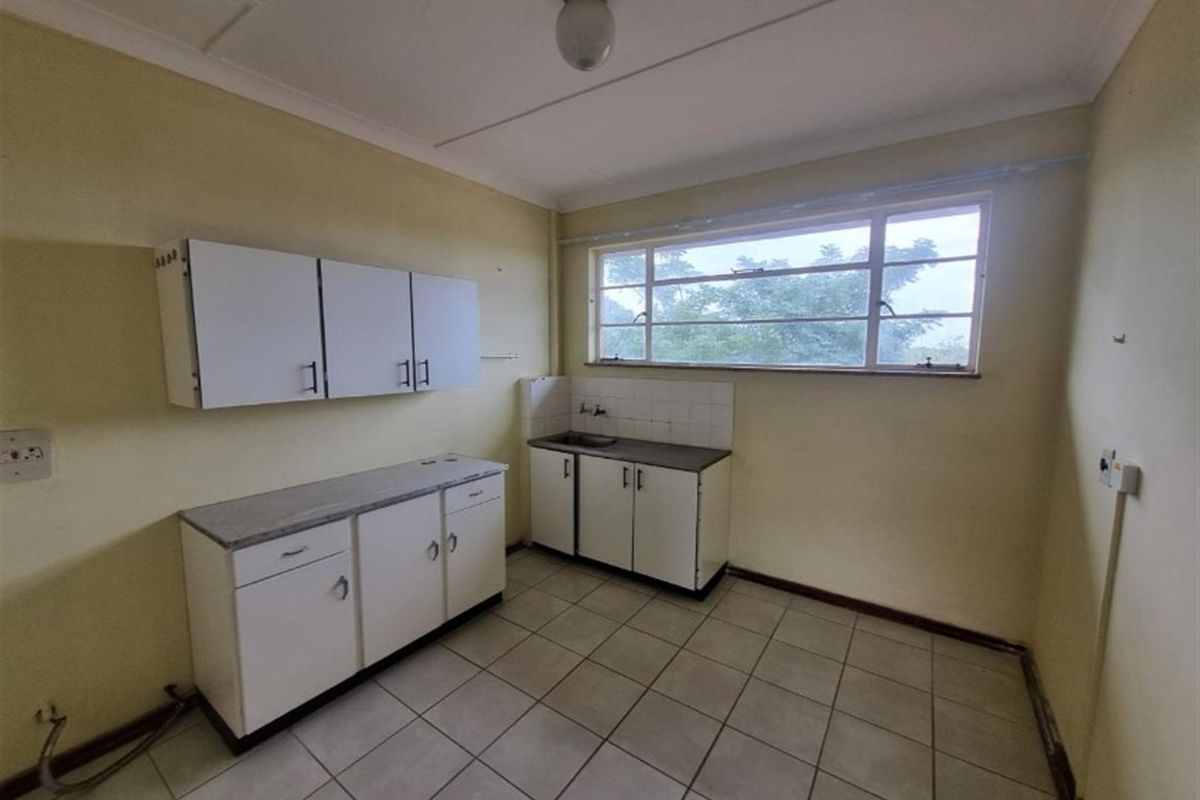 A functional, empty kitchen space featuring basic built-in cabinetry, a stainless steel sink, and tiled flooring, ready for a modern renovation.