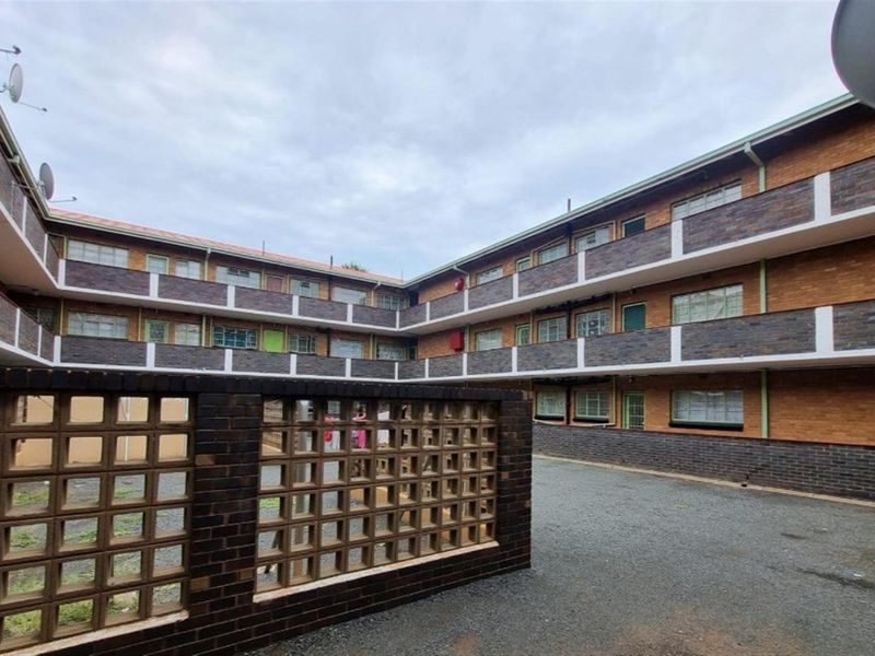 Exterior view of a multi-story residential building featuring brick facade, metal-framed windows, and a central gravel courtyard area.
