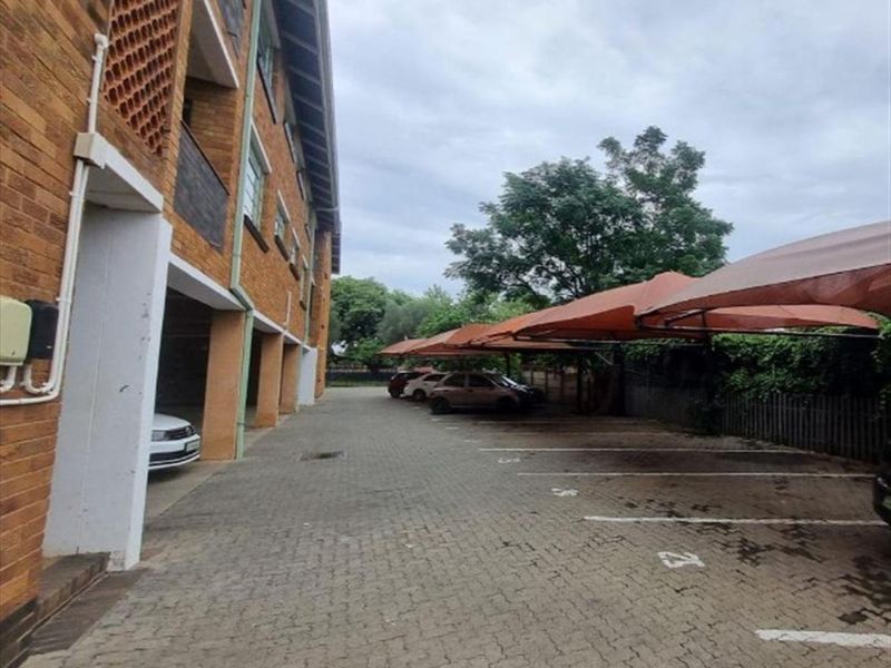 Exterior view of the property featuring a paved driveway with designated parking bays and shade sail carports alongside the brick building facade.