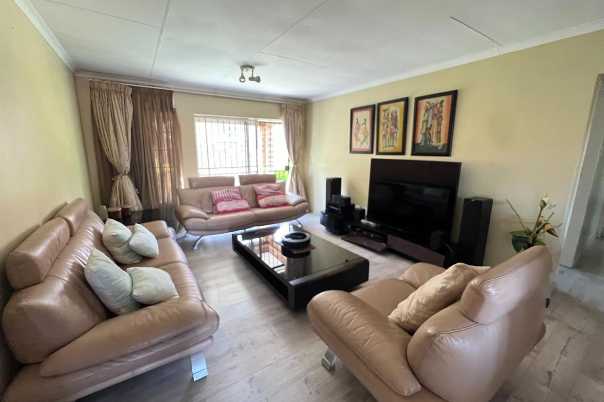 A spacious living room featuring light-toned wood-look flooring and a large window with security bars, providing a comfortable and functional family living space.