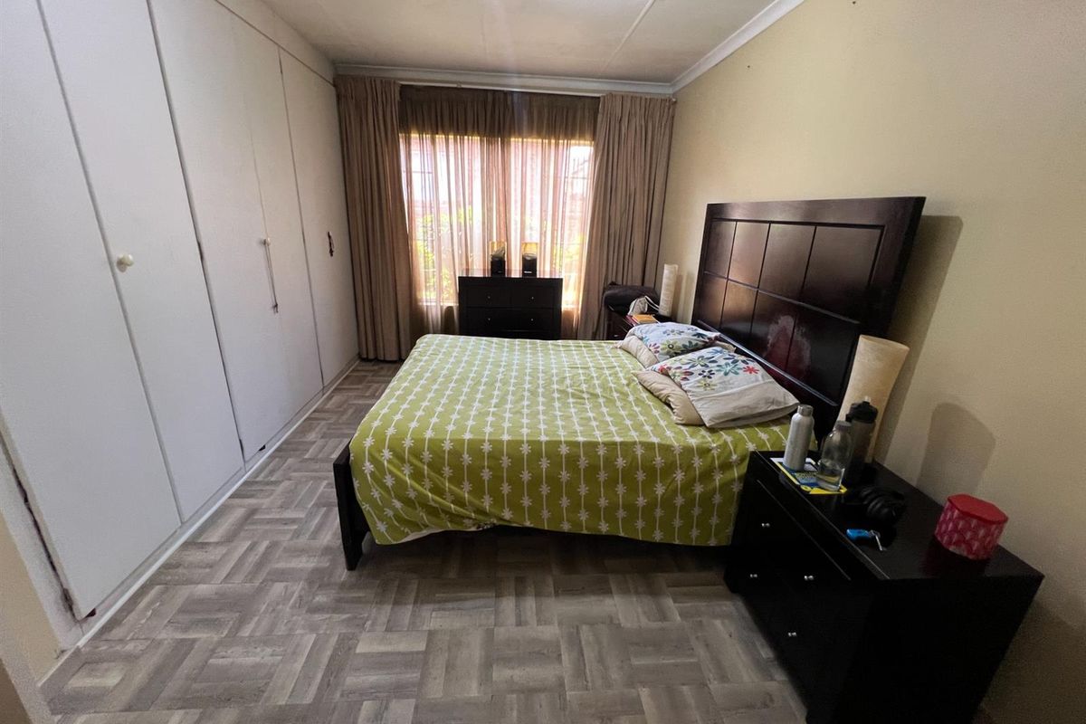 A bedroom featuring built-in floor-to-ceiling wardrobes, patterned vinyl flooring, and large windows with curtains.