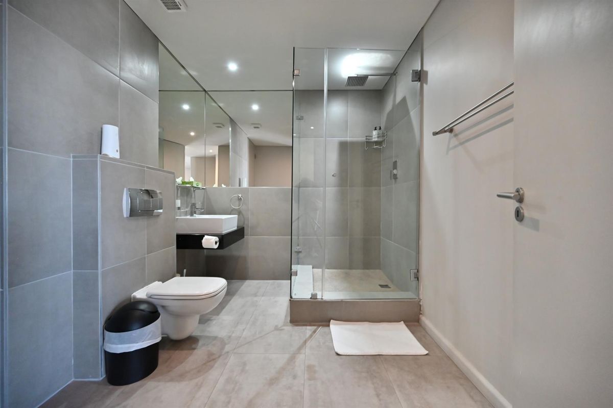 Modern bathroom featuring a glass-enclosed walk-in shower, wall-mounted toilet, and a sleek vanity with a large mirror.