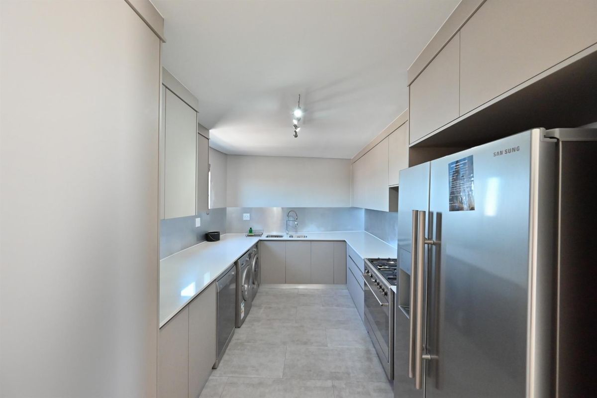 Modern galley-style kitchen featuring sleek cabinetry, stone countertops, stainless steel sink, and integrated space for laundry appliances.