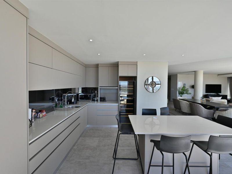 Modern open-plan kitchen featuring sleek handleless cabinetry, stone countertops, integrated wine cooler, and a central island with breakfast bar seating.