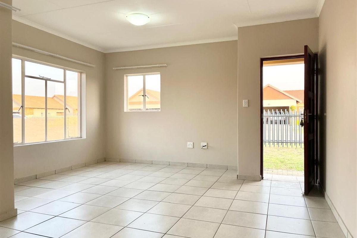 A bright, open-plan living area featuring neutral tiled flooring, large windows for natural light, and direct access to the exterior.