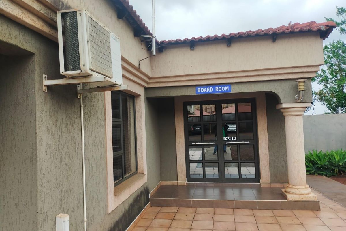 Exterior view of an office building entrance featuring a tiled patio, double glass doors, and an external air conditioning unit.