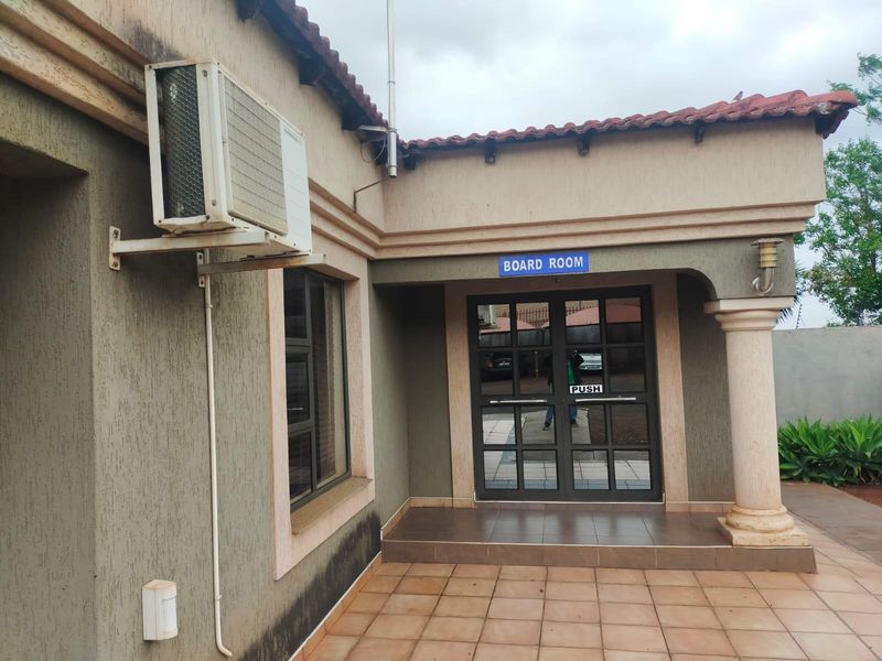 Exterior view of an office building entrance featuring a tiled patio, double glass doors, and an external air conditioning unit.