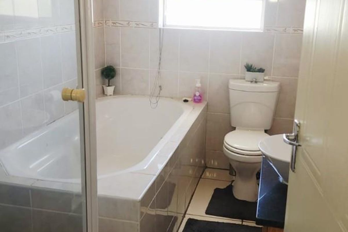 A functional bathroom featuring a built-in bathtub, separate shower enclosure, toilet, and vanity basin with neutral wall and floor tiling.