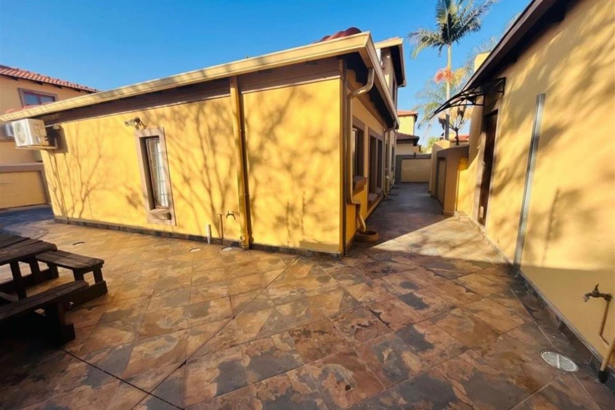 A view of the paved side courtyard and exterior wall of the house, featuring tiled flooring and external drainage fixtures.