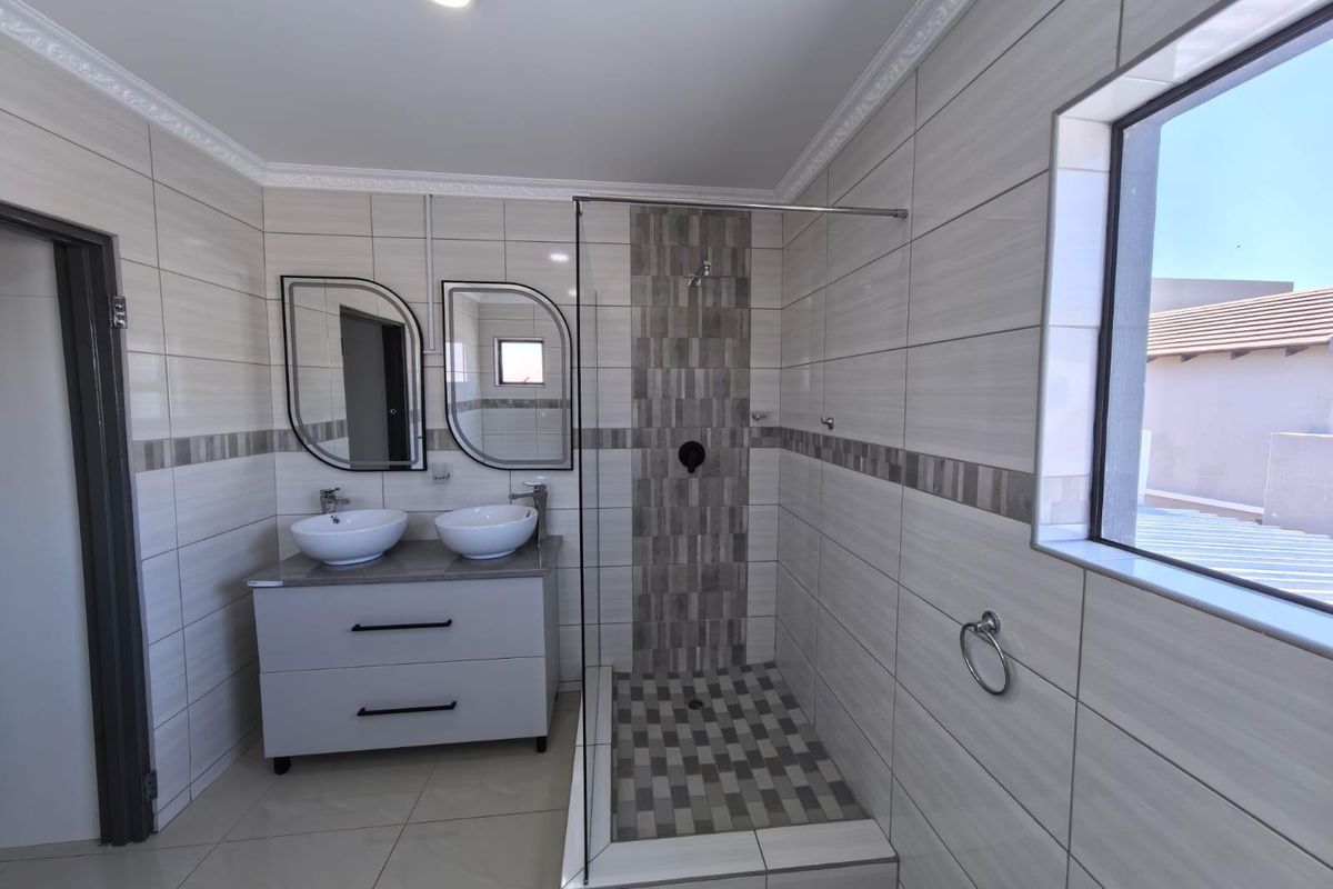Modern bathroom featuring a double vanity with vessel sinks, a walk-in shower with glass enclosure, and contemporary wall tiling.