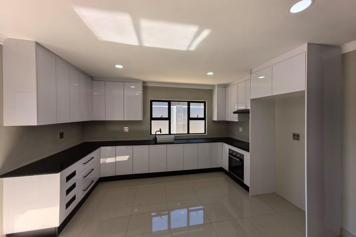 Modern kitchen featuring high-gloss white cabinetry, dark stone countertops, integrated oven, extractor fan, and polished porcelain floor tiles.