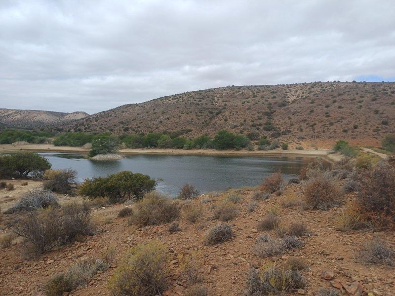 A scenic view of a natural dam or water reservoir surrounded by arid landscape and rolling hills on the farm property.
