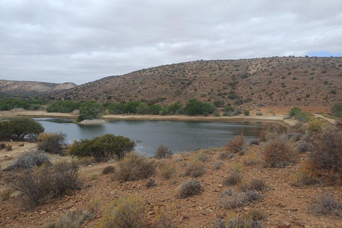 A scenic view of a natural dam or water reservoir surrounded by arid landscape and rolling hills on the farm property.