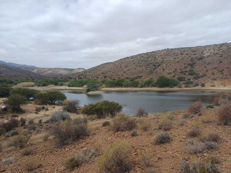 A scenic view of a natural dam and surrounding arid landscape on the farm property.