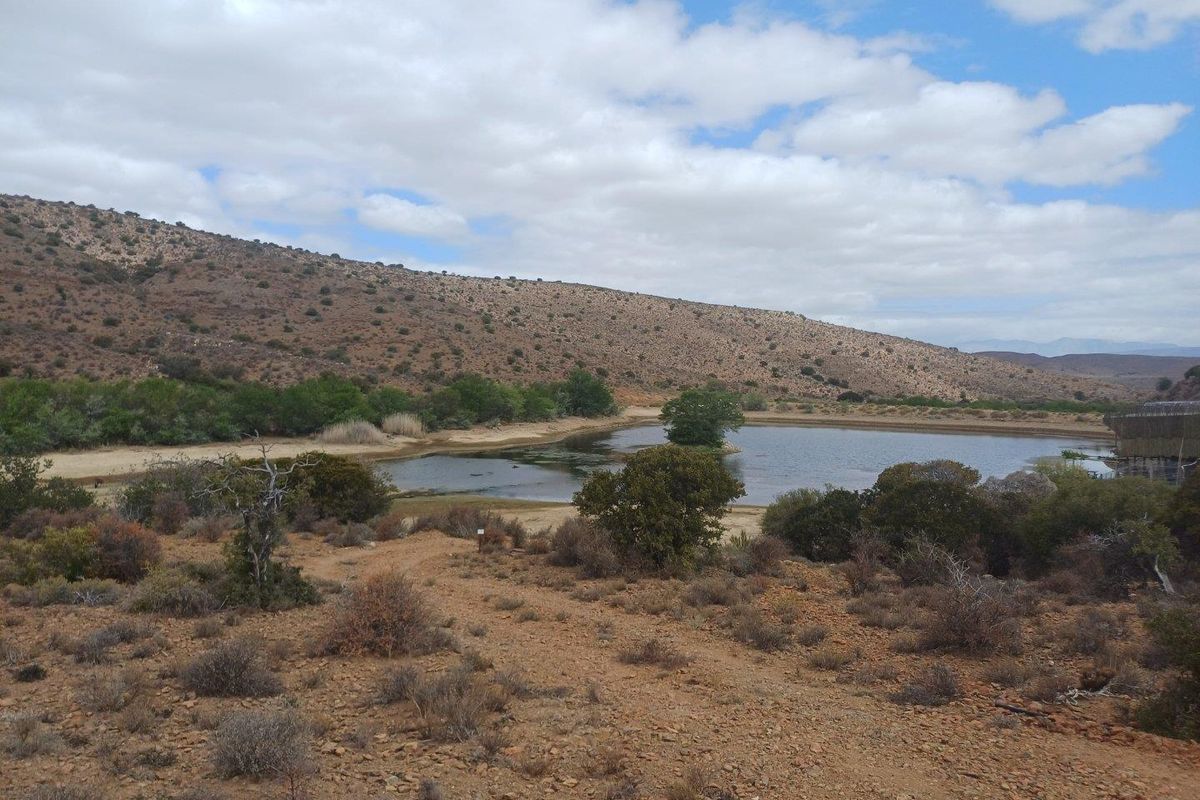 A scenic view of a natural farm dam surrounded by arid landscape and rolling hills under a partly cloudy sky.