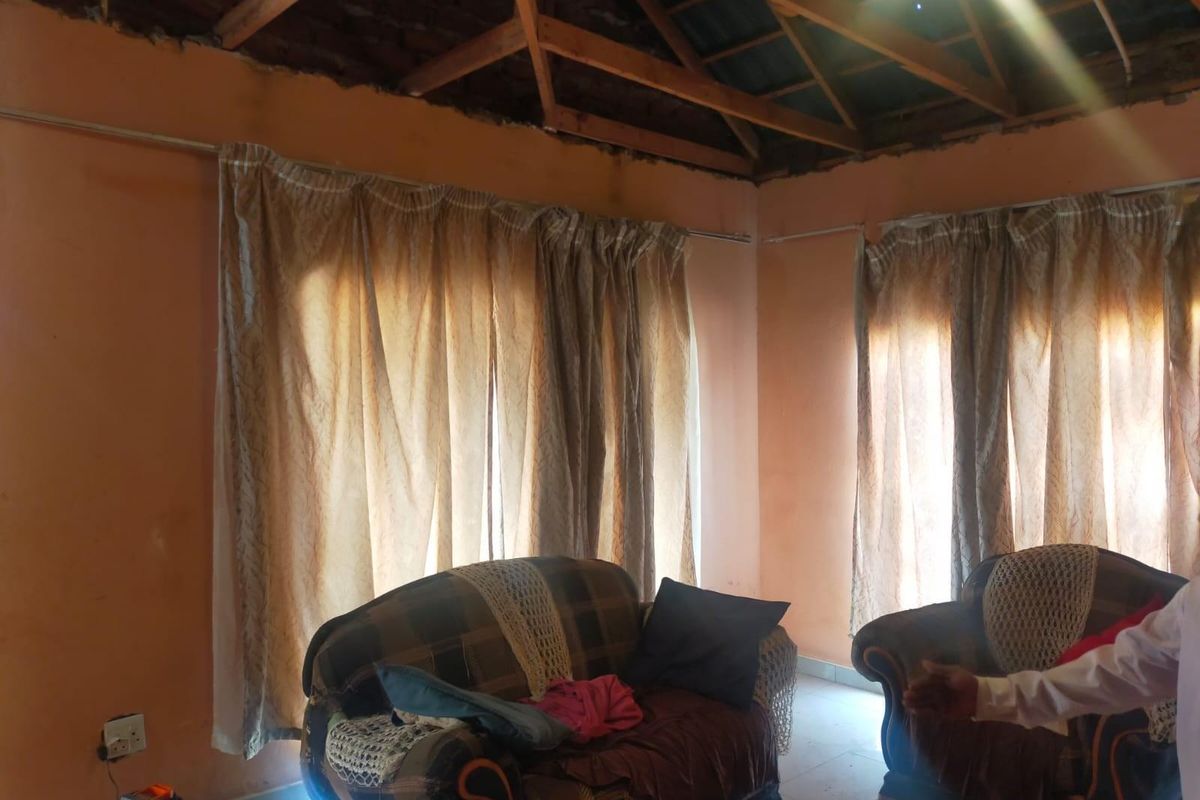 Living area featuring exposed timber roof trusses and unfinished ceiling, requiring significant renovation and cosmetic repairs to the walls and interior finishes.