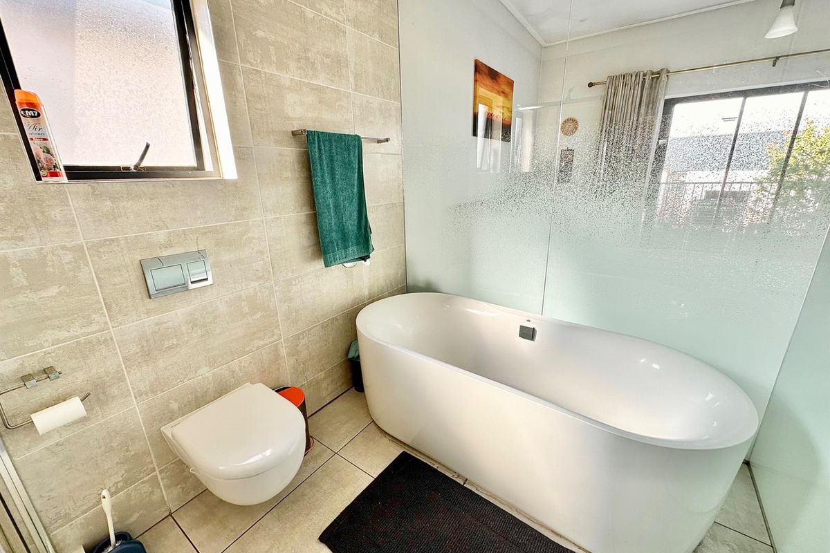 Modern bathroom featuring a sleek freestanding bathtub, wall-mounted toilet with concealed cistern, and contemporary neutral wall tiling with a frosted glass privacy screen.