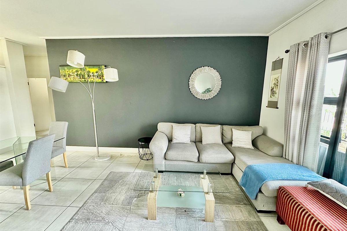 A bright living room featuring tiled flooring, a dark grey feature wall, and a sliding glass door providing natural light.