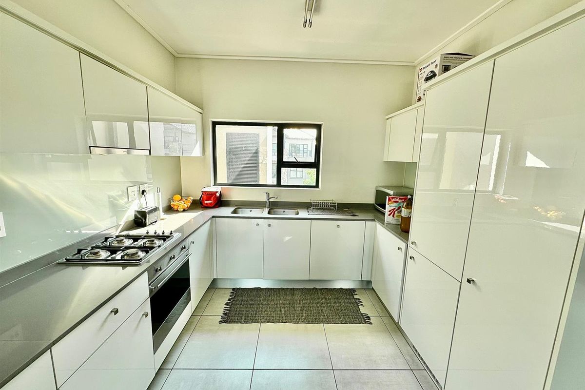 Modern galley-style kitchen featuring high-gloss white cabinetry, stone countertops, integrated gas hob, electric oven, and tiled flooring with ample natural light.