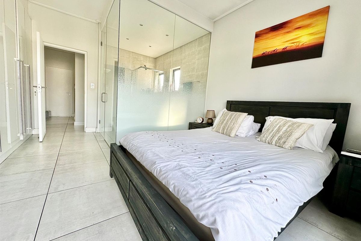 Modern bedroom featuring tiled flooring, built-in storage, and a contemporary glass-enclosed en-suite bathroom with recessed lighting.