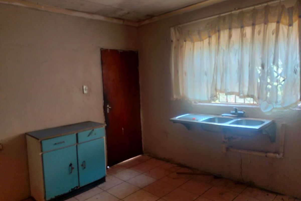 A basic kitchen area featuring a stainless steel double sink, tiled flooring, and a single built-in base cabinet, requiring significant renovation and cosmetic updates.