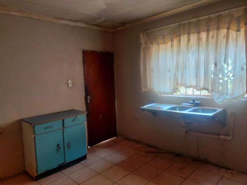 A basic kitchen area featuring a stainless steel double sink, tiled flooring, and a single built-in base cabinet, requiring significant renovation and cosmetic updates.