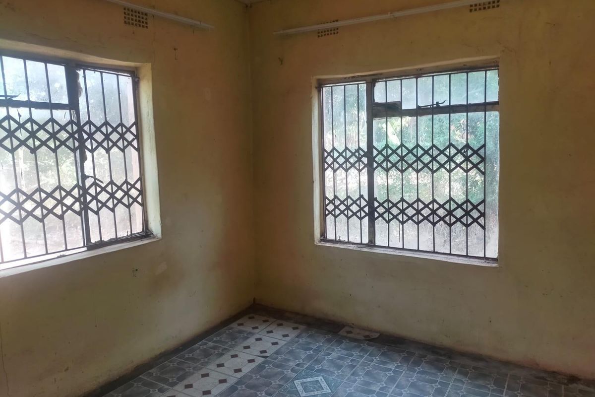 An empty bedroom featuring tiled flooring and security gates on the windows, requiring cosmetic updates and painting to restore its condition.