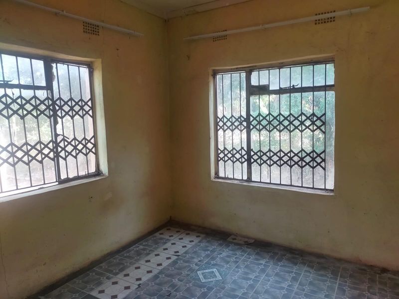 An empty bedroom featuring tiled flooring and security gates on the windows, requiring cosmetic updates and painting to restore its condition.