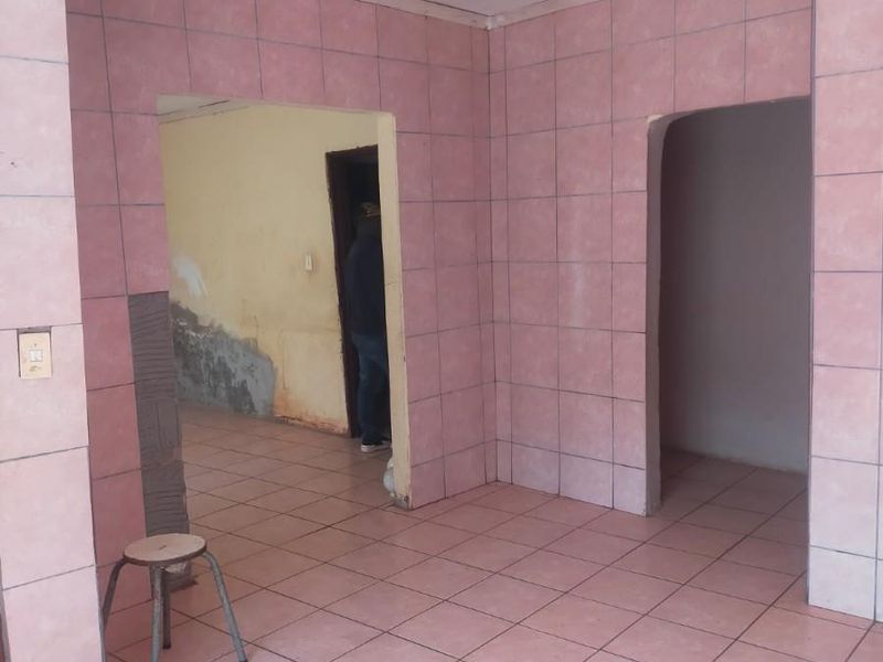 An empty living area featuring pink wall and floor tiles, showing signs of wear and requiring cosmetic updates to the wall finishes.