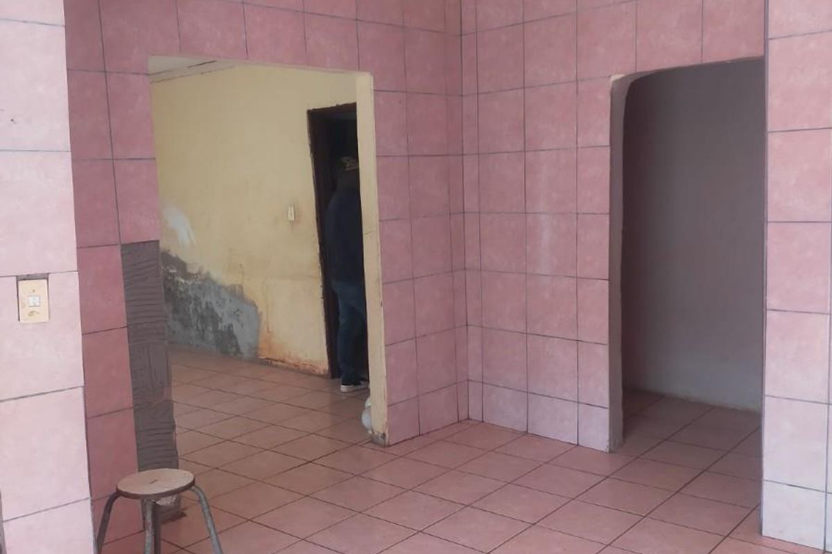 An empty living area featuring pink wall and floor tiles, showing signs of wear and requiring cosmetic updates to the wall finishes.