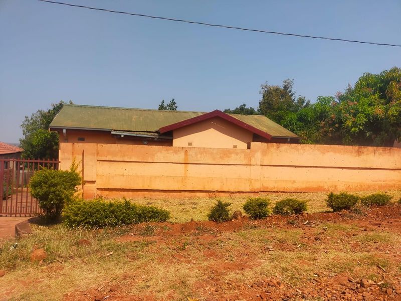 Front view of a residential property featuring a corrugated metal roof and a solid perimeter boundary wall with an access gate.