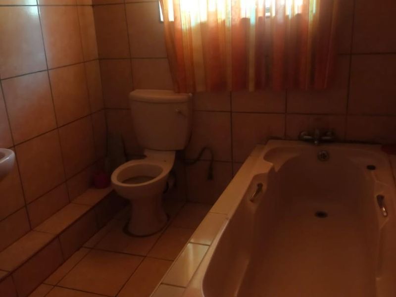 A dated bathroom featuring a built-in bathtub, toilet, and basin with full-height wall tiling and floor tiles.
