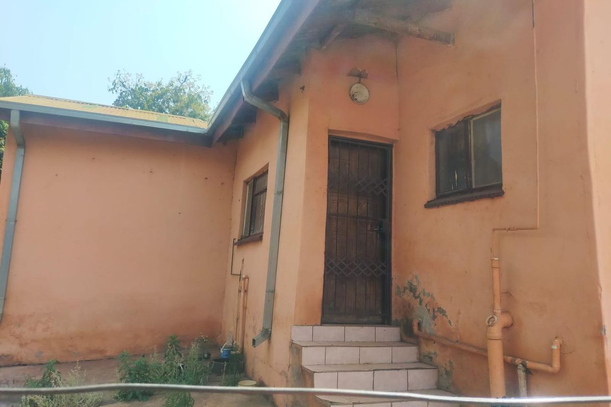 Rear exterior view of the house showing tiled entrance steps, security gate, and weathered wall finishes requiring maintenance.