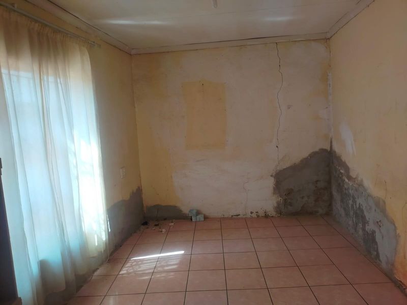 An empty bedroom featuring tiled flooring and a curtain rail, currently requiring significant wall repairs and plaster restoration.