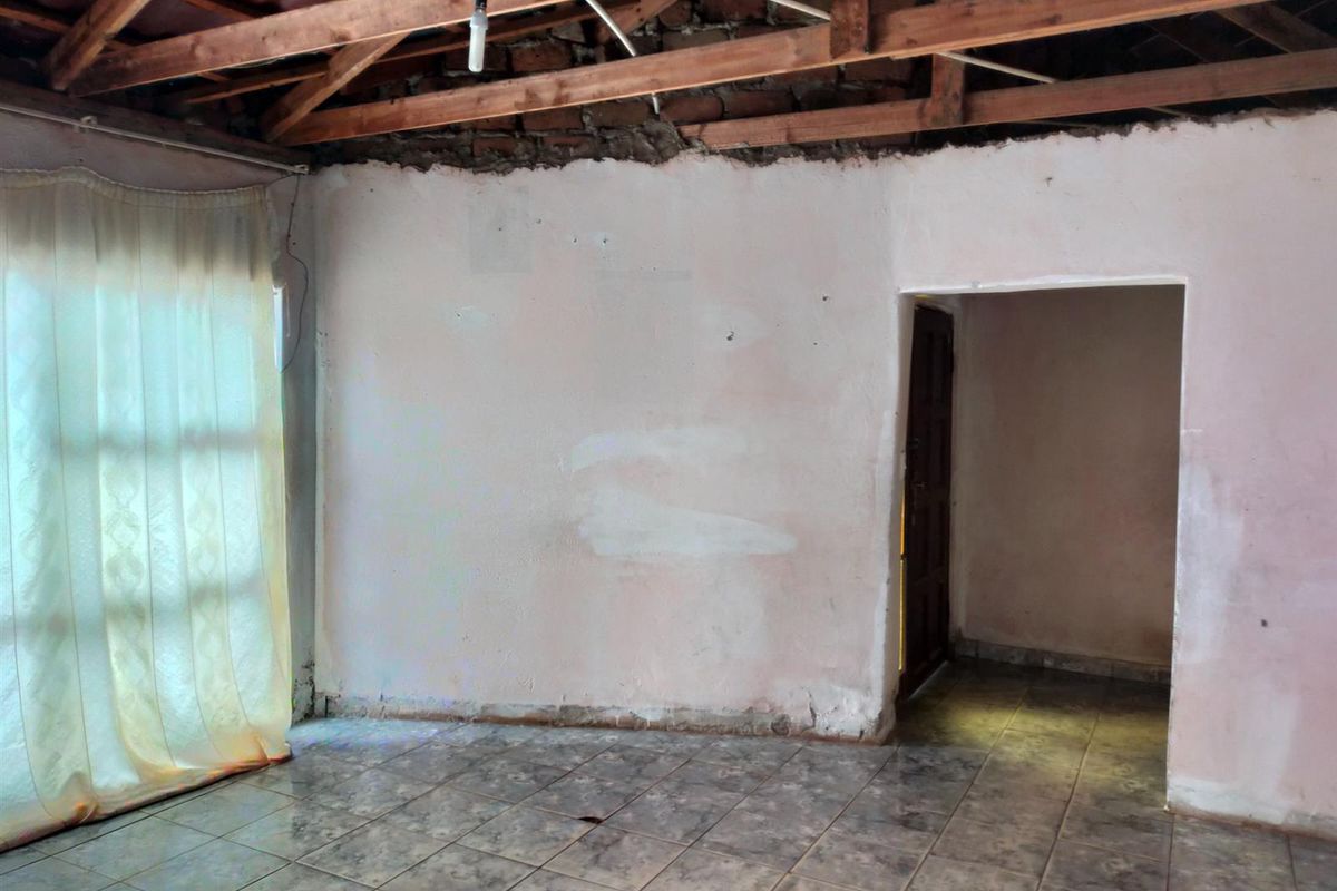 An unfinished interior room featuring exposed timber roof trusses, raw wall finishes, and tiled flooring, offering a blank canvas for renovation.