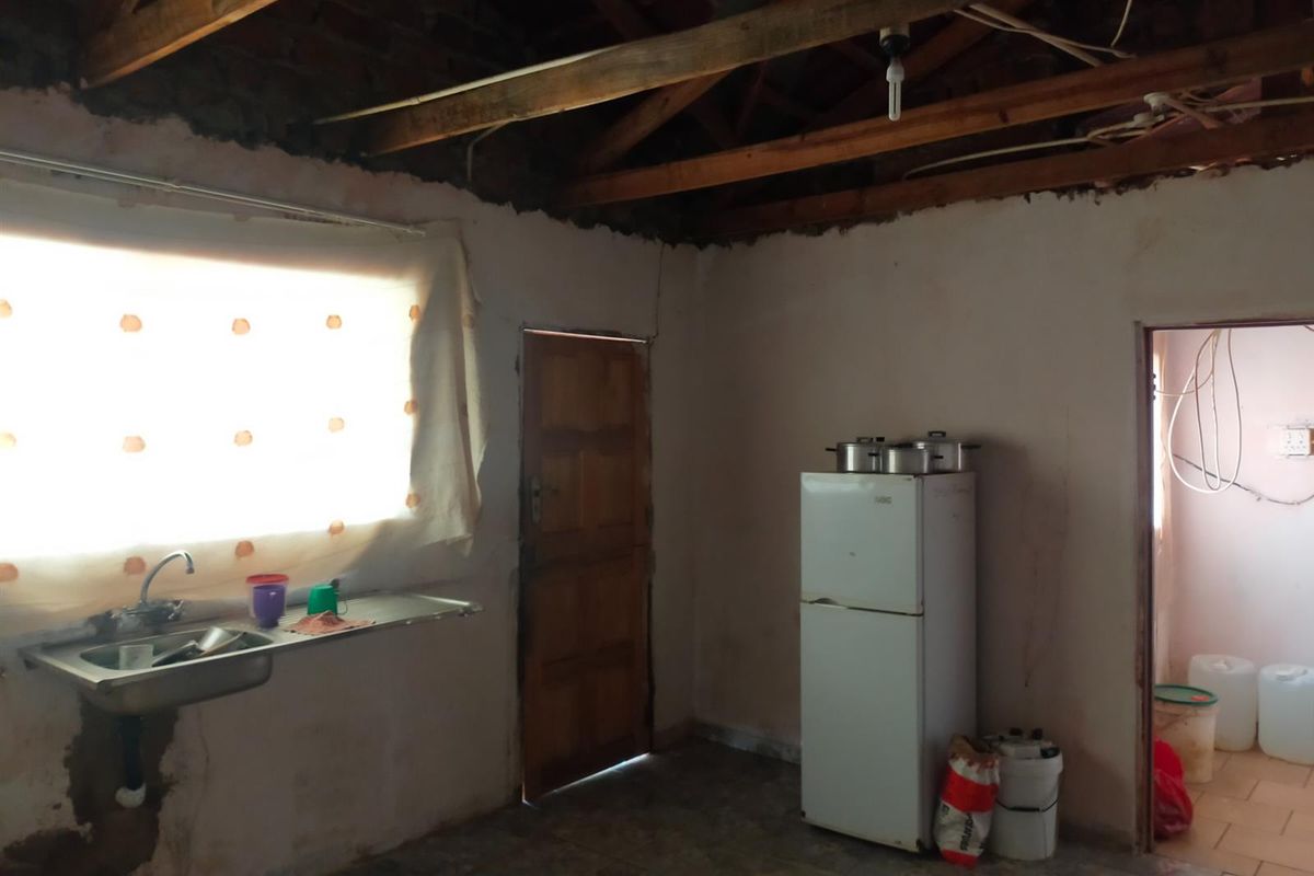 A basic kitchen area featuring a stainless steel sink, exposed timber roof trusses, and unfinished wall surfaces, requiring significant renovation and finishing work.