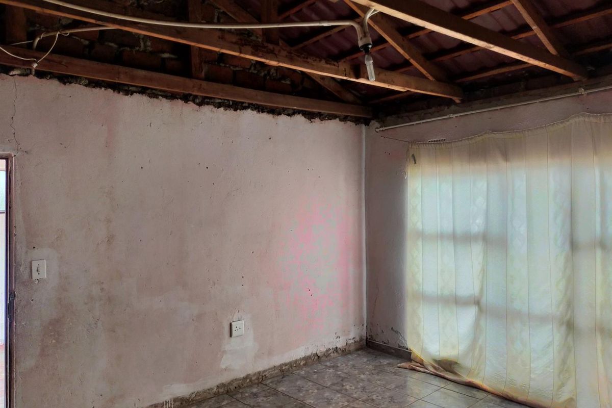 An interior room featuring exposed timber roof trusses, tiled flooring, and unfinished wall surfaces requiring significant renovation and repair.