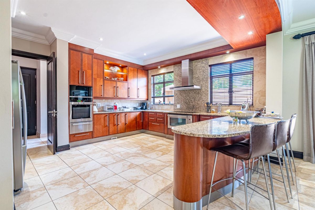 Spacious kitchen featuring warm wood cabinetry, granite countertops, a central breakfast island, built-in oven, and stainless steel extractor fan.
